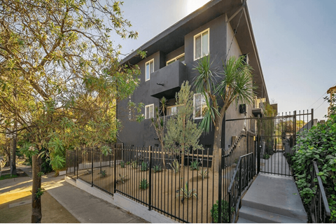 A modern house with a black fence and a tree in front.