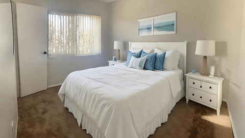 A bedroom with a large bed, a nightstand, and a window with curtains.