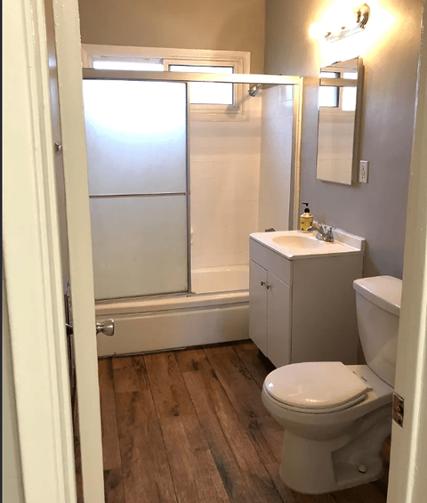 A white toilet in a bathroom with a white fridge in the background.