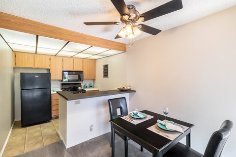 A kitchen with a black fridge and a black dining table with two chairs.