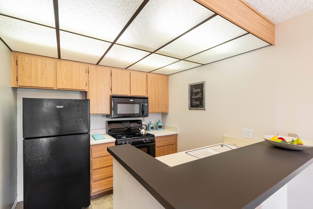 A black refrigerator is in a kitchen with wooden cabinets at Chaparral Apartments, Palmdale, CA, 93551