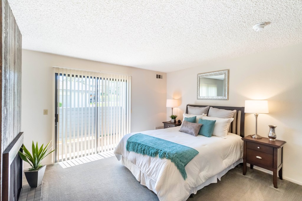 A bedroom with a large bed and a balcony with a sliding door at Chaparral Apartments, Palmdale 93551