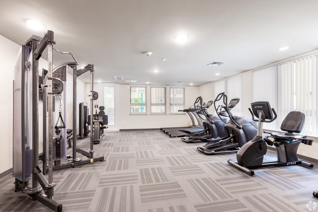 A well-lit gym with a variety of equipment including treadmills, stationary bikes, and weight machines.
