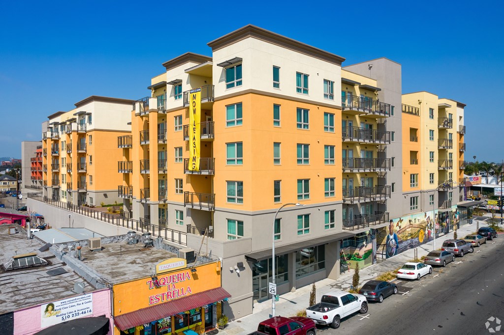 A street view of a yellow and white apartment building with cars parked in front.