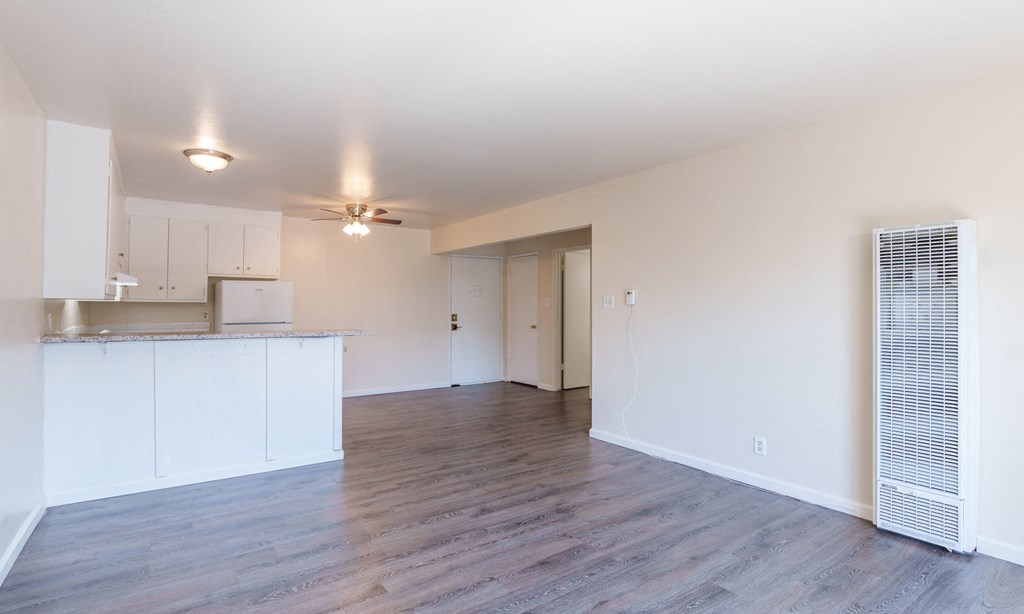 an empty living room and kitchen with white walls and wood flooring