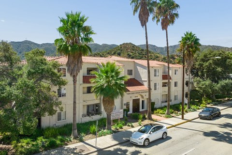 A white car is parked on the street in front of a building with a red tile roof.