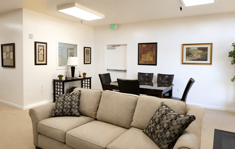 A beige couch with two pillows sits in a room with a white wall and a painting hanging on it.
