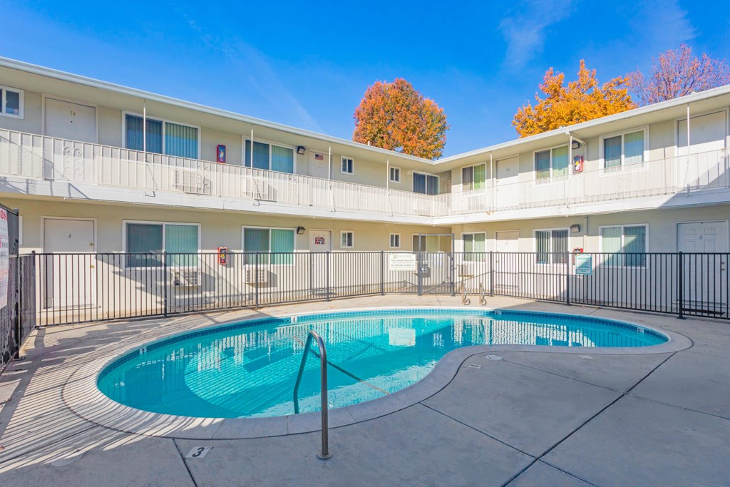 A swimming pool is surrounded by a black fence in front of a white building.