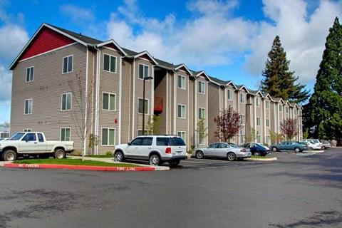 A row of apartment buildings with cars parked in front.