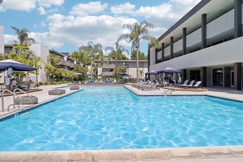 A large swimming pool with lounge chairs and umbrellas in front of a building.
