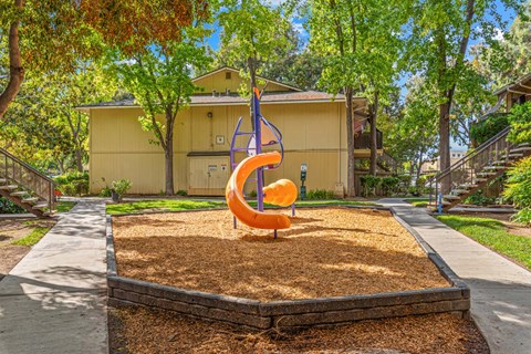 A playground with a slide in the middle of a sandbox.
