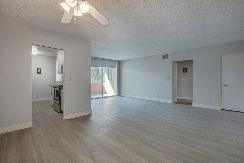 A spacious living room with a ceiling fan and lighting fixture.