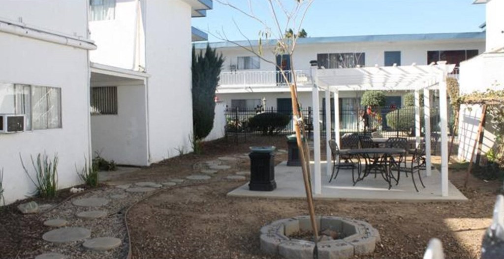 A patio with a table and chairs is surrounded by white buildings.