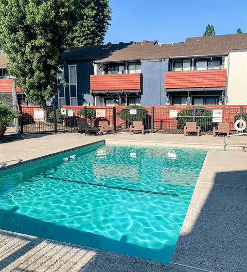 A swimming pool in front of a building with red and grey balconies.