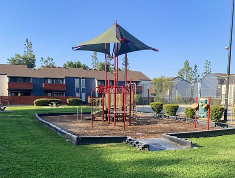 A playground with a red and blue umbrella and a slide.