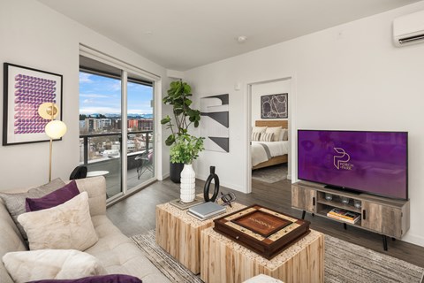 a living room with white walls and a large window with a bed in the background