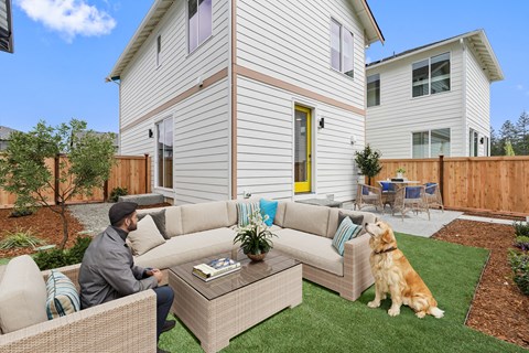 A man is sitting on a couch with a dog on the lawn.