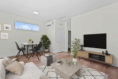A modern living room with a grey sofa, a wooden coffee table, a black TV, and a white wall with a window.
