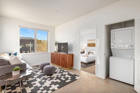 a living room with a washer and dryer and a bedroom with a bed