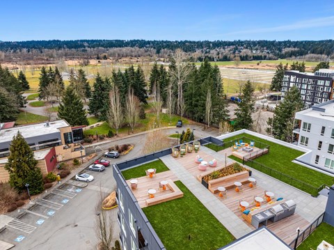 A rooftop patio with a table and chairs overlooks a parking lot and trees.