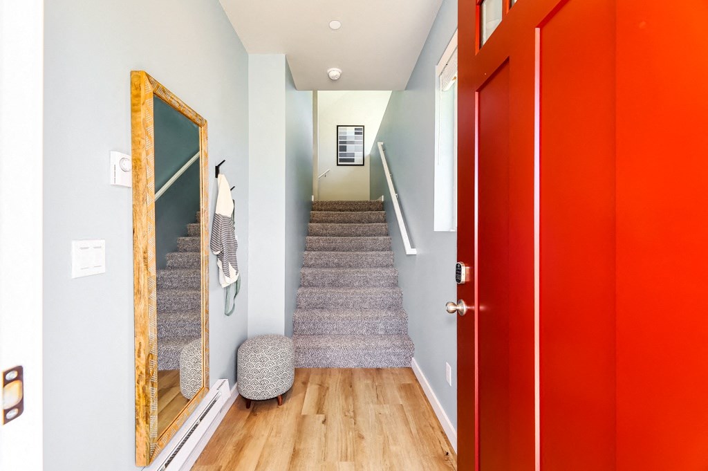 a red door opens up to a staircase with grey carpet and a large mirror on the wall