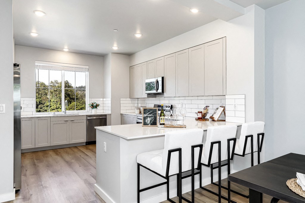 a kitchen with white cabinets and a white island with three white chairs
