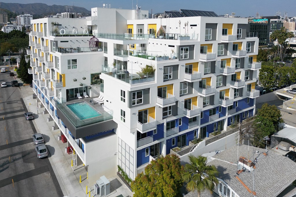 an aerial view of a white building with blue and yellow windows and a pool in front of