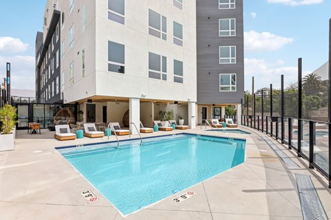 A large swimming pool is surrounded by lounge chairs and a building.