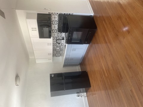 A black refrigerator and stove in a kitchen with wooden floors.
