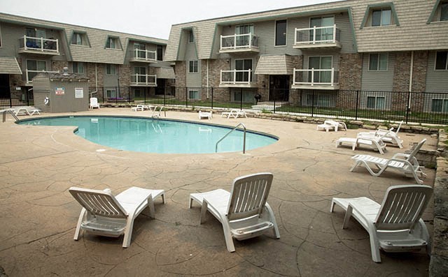 a swimming pool with chairs in front of an apartment building