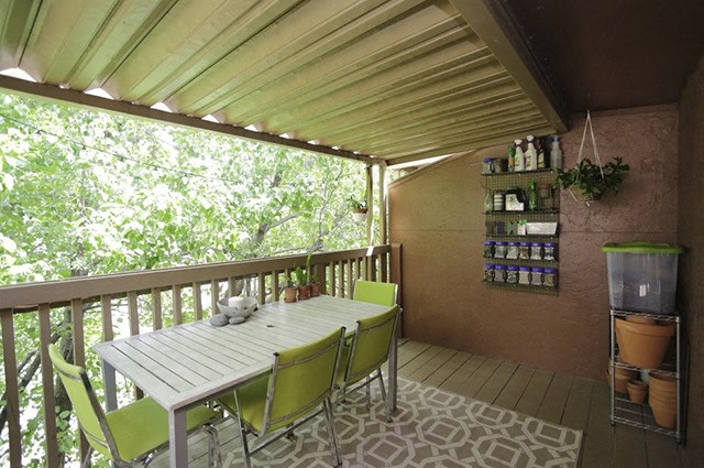 a covered patio with a white table and green chairs