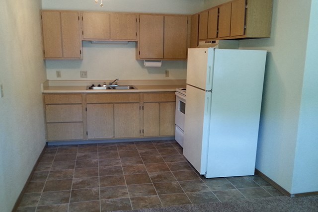 an empty kitchen with a refrigerator and cabinets