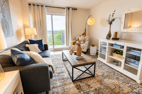 A living room with a grey couch, a coffee table, and a large window with curtains.