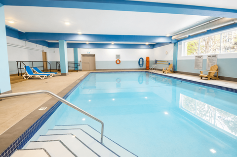A large indoor swimming pool with a blue tiled edge and a metal ladder.