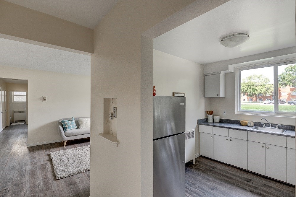 the view of a kitchen and living room from a hallway with a refrigerator and sink