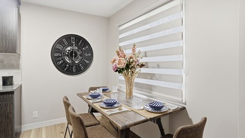 A dining room with a table set for two and a clock on the wall.