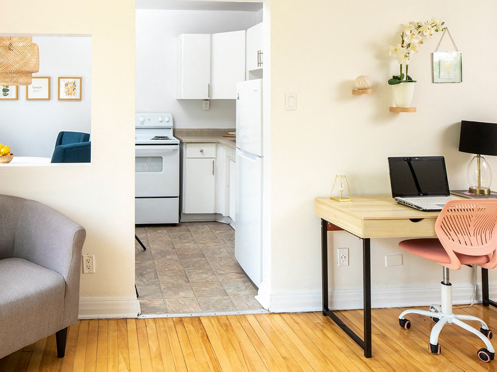 a home office with a laptop computer on a desk and a kitchen