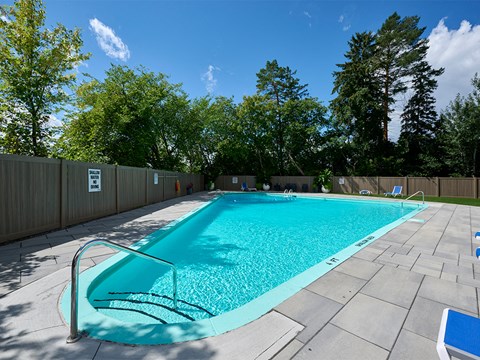 A rectangular pool with a metal railing and a blue bench.