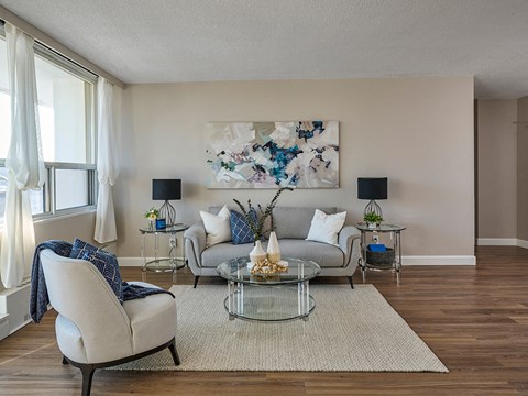 A living room with a grey couch, a glass table, and a painting on the wall.