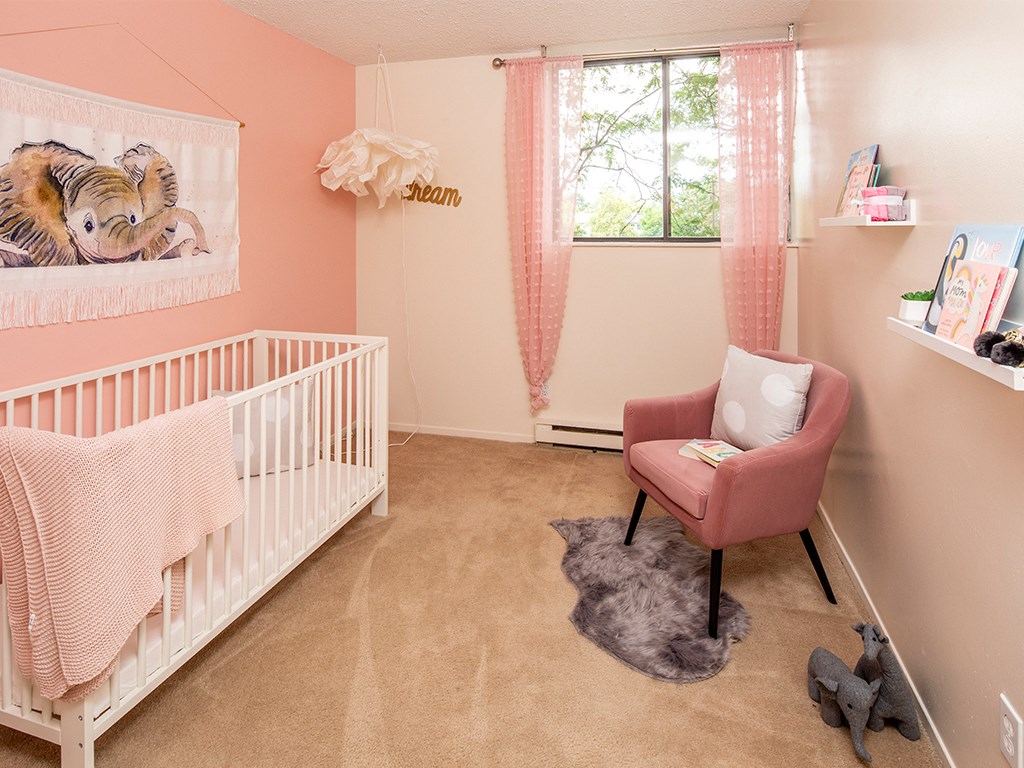 a pink and white nursery with a crib and a pink chair
