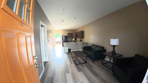 A living room with a black couch and a wooden floor.
