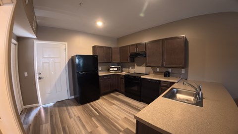 A kitchen with a black refrigerator and brown cabinets.