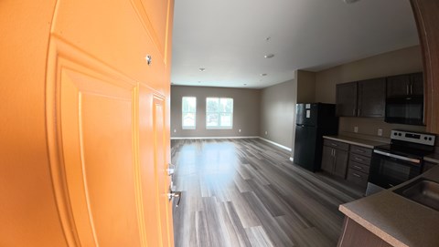 A kitchen with wooden floors and a black trash can.
