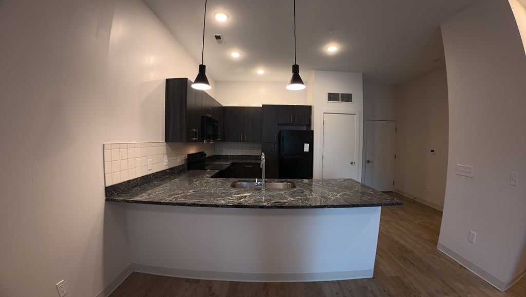 A kitchen with a granite countertop and a black fridge.