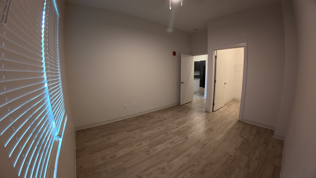 A room with a wooden floor and a white wall with a doorway leading to another room.