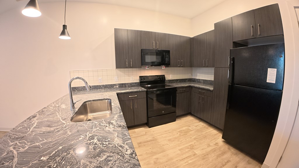 A kitchen with black appliances and a marble counter top.