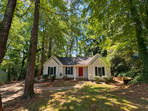 A small white house with a red door is surrounded by trees.