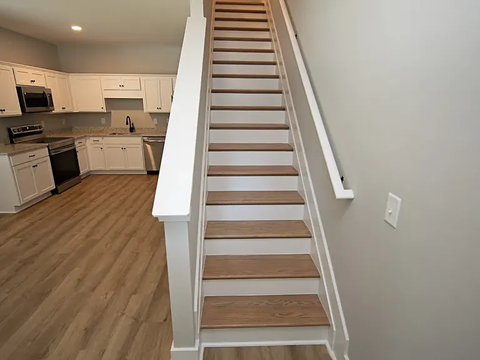 A staircase with wooden steps and white railings leads up to a kitchen area.