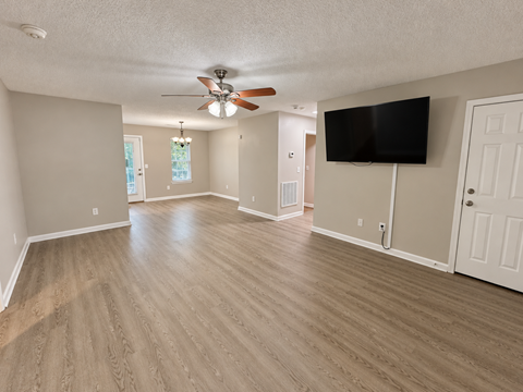 A spacious room with a ceiling fan and a flat screen TV mounted on the wall.