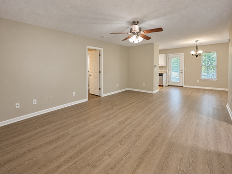 A room with a ceiling fan and light fixture, wooden flooring, and a doorway leading to another room.